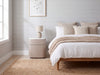 Arca curved bedside table beside a bed with neutral bedding in a modern Dubai bedroom