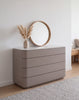 Arca rounded chest of drawers in taupe with stone top, styled with a round mirror in a bedroom
