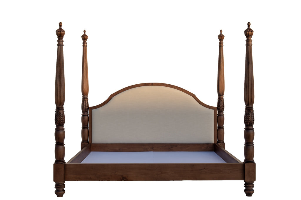 Close front view of carved four poster bed with ivory linen upholstered headboard framed in walnut