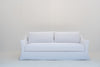 White linen slipcovered sofa with flared slope arms and kick-pleat skirt, front view