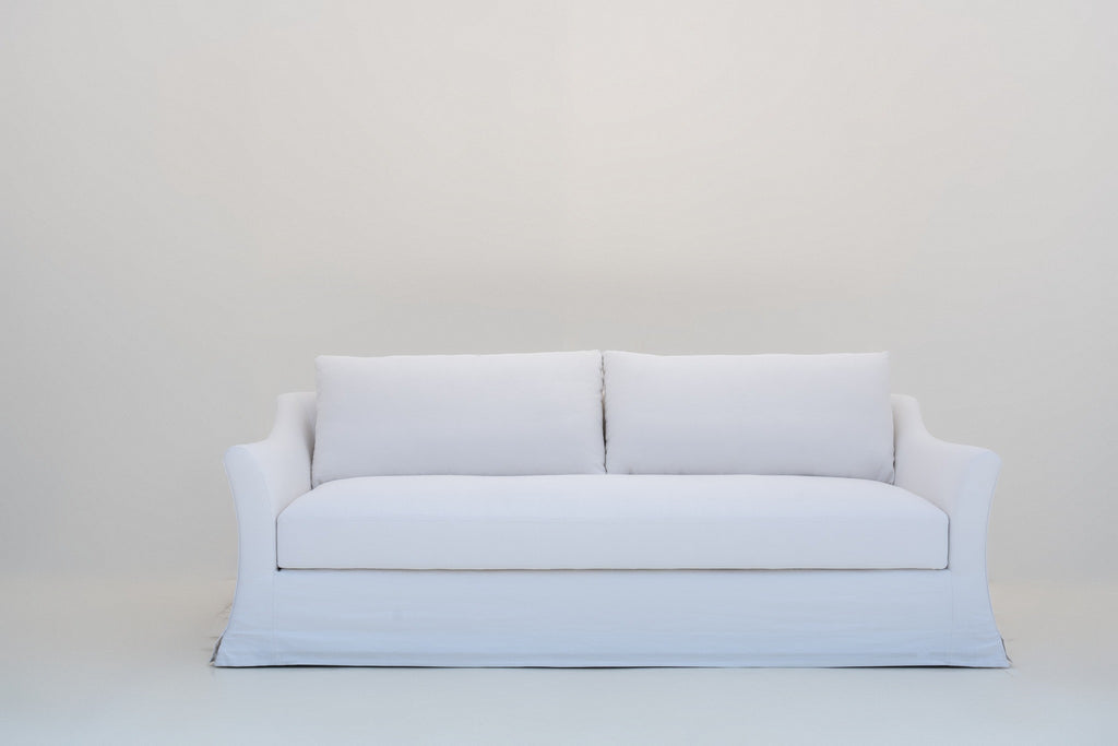 White linen slipcovered sofa with flared slope arms and kick-pleat skirt, front view