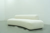 Dune curved sofa side angle showing the sweeping arc and recessed black plinth base