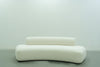 Modern curved sofa in ivory bouclé on a floating black plinth, front view
