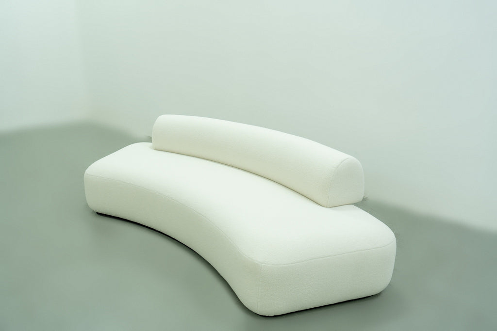 White bouclé sofa with a sweeping curved seat and offset bolster backrest