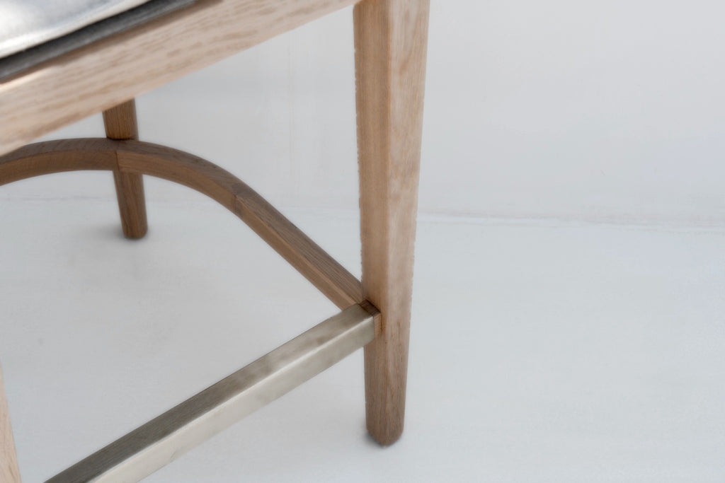 Close-up of the tapered oak legs, curved oak footring and brushed brass footrest